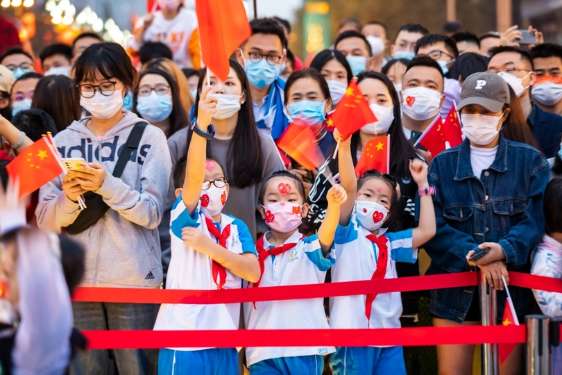 一群戴着口罩、举着中国国旗的人排在街道两旁