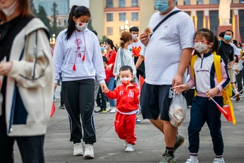 当一群人走过时 一个戴着口罩的小女孩在街上奔跑