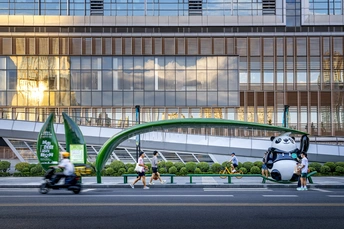 人们穿过街道 前面是一座大型办公楼 一只巨大的熊猫骑着桥而过。