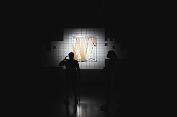 一个男子和一个女子站在一个黑暗的房间里 墙上投影着艺术作品。男子在墙上投下了一个影子。