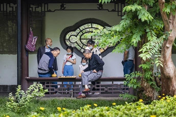 一个男人和一个小男孩坐在一条长凳上 长凳在建筑物的正面 前面有一棵树。