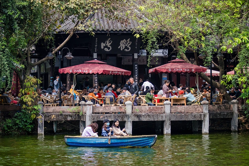 一艘小船在水上 许多人坐在有遮阳伞的桌子旁。