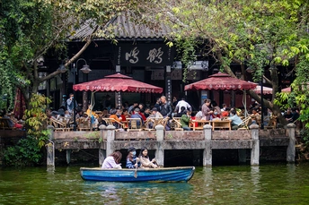 一艘小船在水上 许多人坐在有遮阳伞的桌子旁。