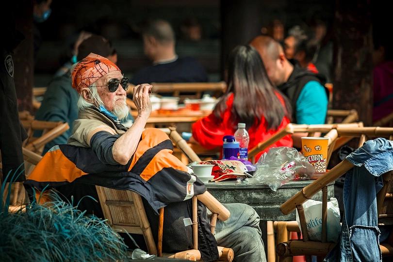 一个老人坐在户外的餐厅的椅子上吃食物。