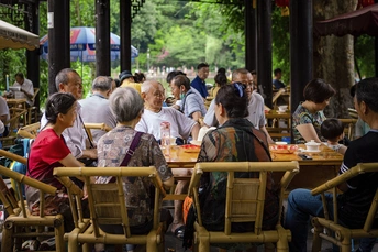 人们坐在户外桌子旁 有遮阳伞 正在吃食物。