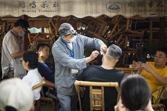 一个戴面具的男子正在由理发师剪发的过程中 理发师坐在人群前面的一把椅子上。