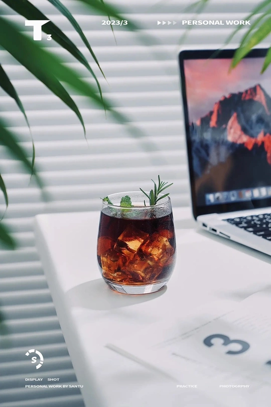 一杯饮料放在桌子上的电脑旁边 旁边还有一盆植物。