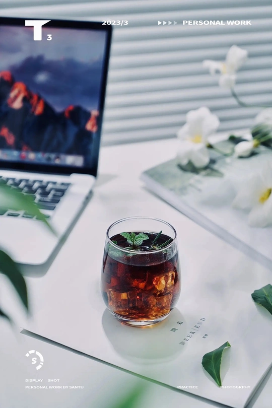 一杯茶放在一个白色的桌子上 旁边是一台电脑和一盆有花的植物。