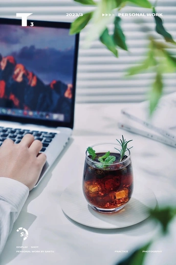 一个在桌子旁的女人 手拿笔记本电脑 手边还有一杯茶和一杯鸡尾酒。