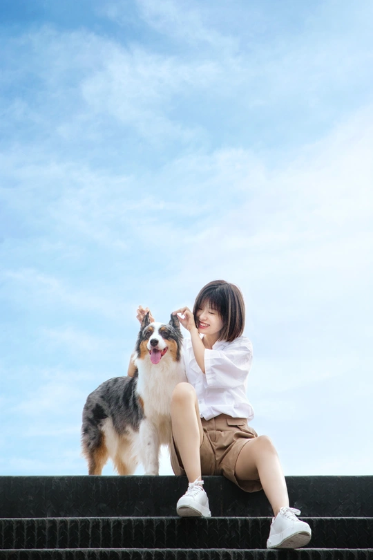 一个年轻女子和一只小狗在蓝天下的台阶上坐着