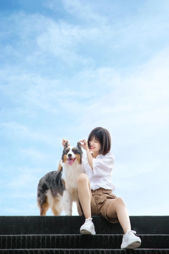 一个年轻女子和一只小狗在蓝天下的台阶上坐着