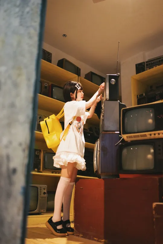 一个穿着白色连衣裙的年轻女子站在一个杂乱无章的房间里 面前是一台电视。