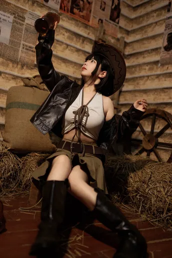 一个穿着黑色连衣裙和靴子的女人坐在干草上 带着枪和帽子。