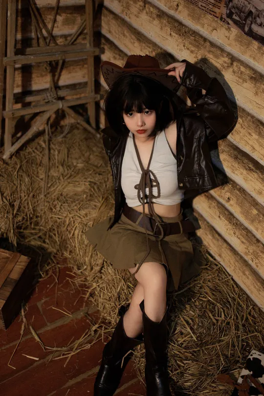 一个穿着黑色靴子和黑色帽子坐在谷仓里的女人