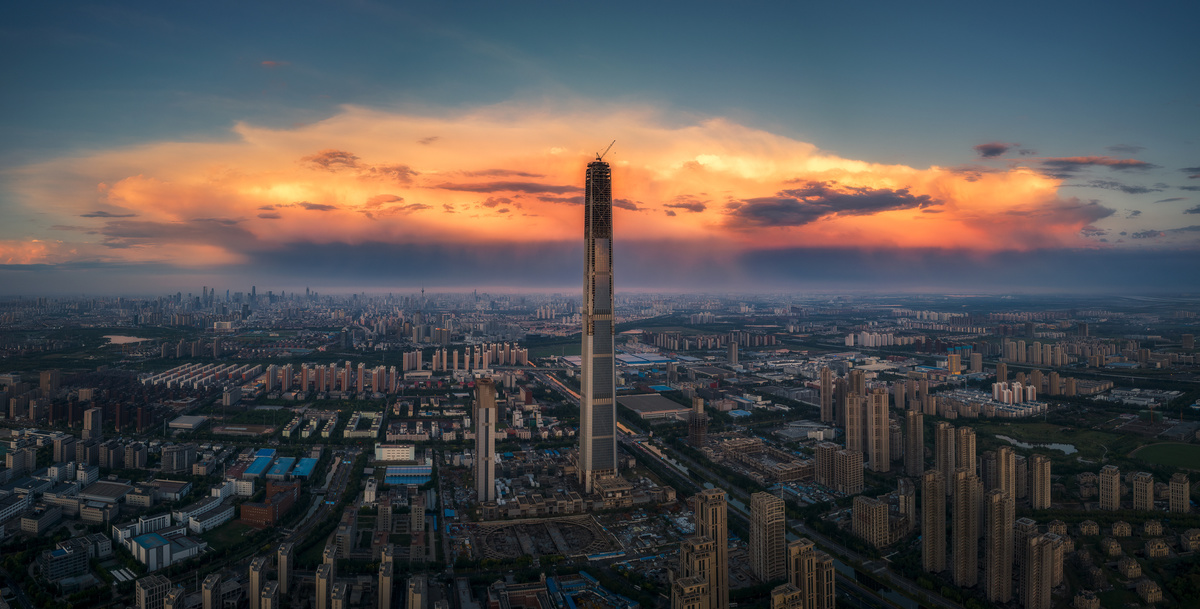 夕阳下城市的 aerial view 天空中有大云朵 顶部有一座高塔。