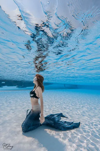 一位穿着比基尼的年轻女子坐在蓝色泳池的表面。