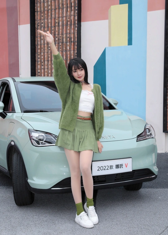 一位穿着绿色裙子的年轻女子站在一辆车前