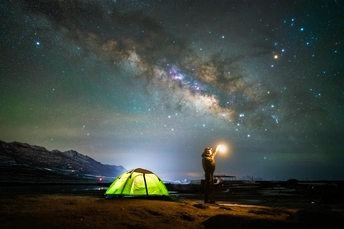 晚上 一个拿着手电筒的女人站在绿色帐篷旁看着天空中的星星