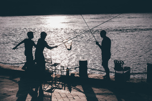 一个男子和一些男孩站在码头上在夜间钓鱼靠近水