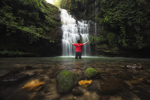 一位穿红衬衫的男子站在森林中的瀑布前