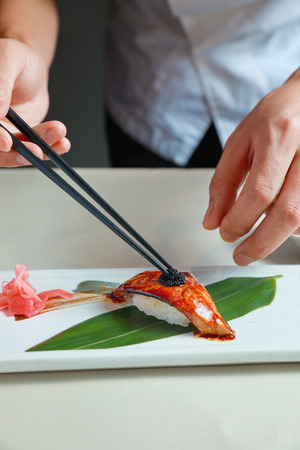 一个人用筷子夹在一盘寿司上的手