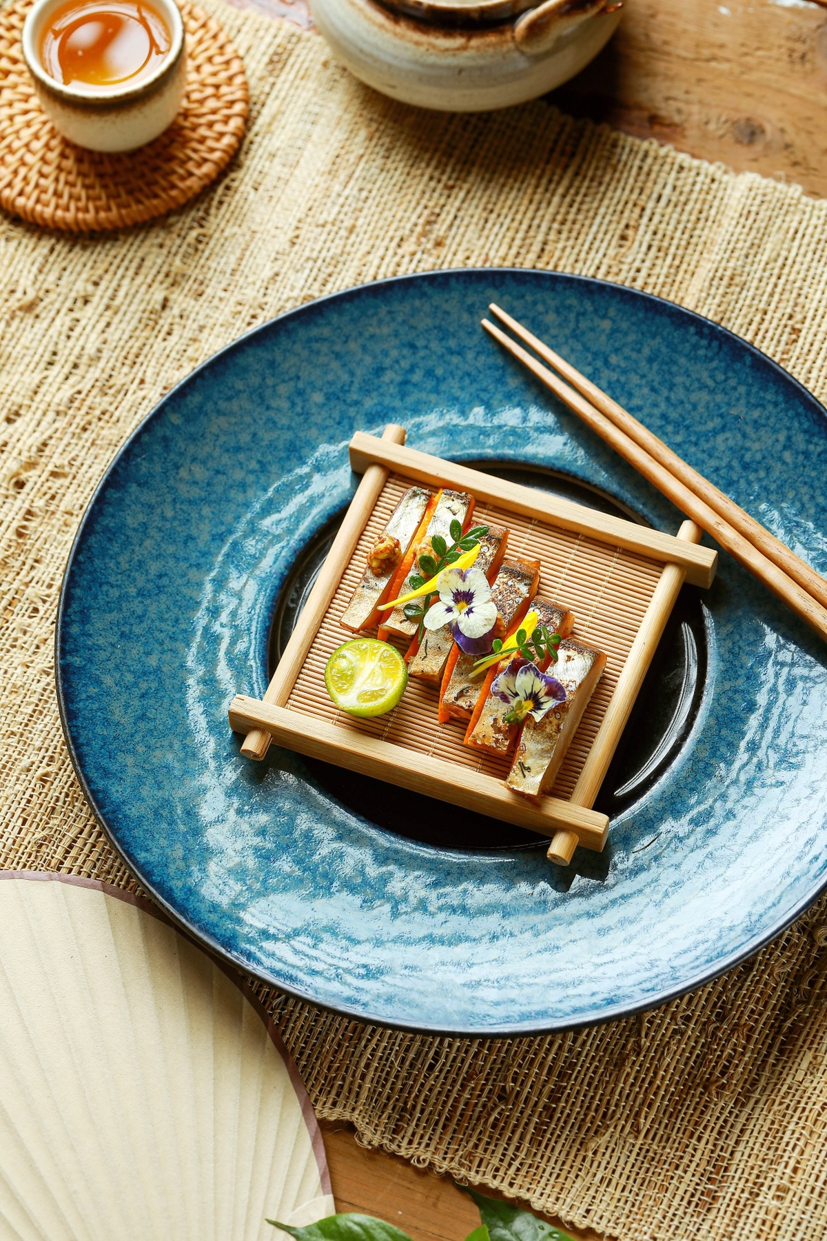 一个小碗寿司 放在蓝色的盘子上 配有筷子和一杯茶。