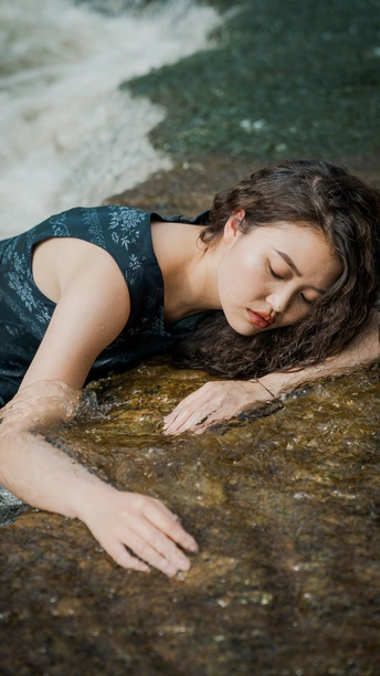一位头发美丽的年轻女子躺在溪流中的岩石上