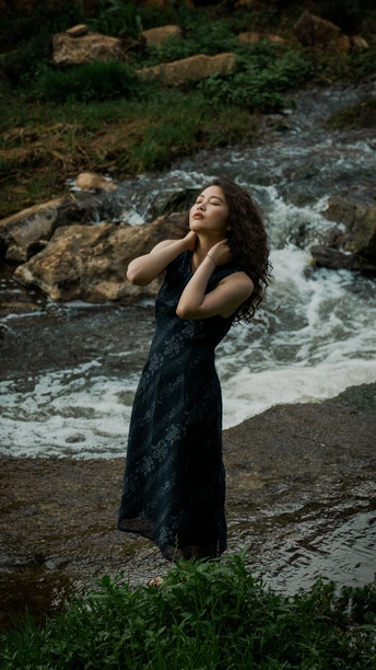 一位身穿黑色连衣裙的年轻美女撑着雨伞在溪流前摆姿势