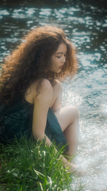 一个美丽的年轻女子坐在小溪边的草地上