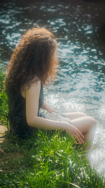 一个年轻的女人坐在草地上的小溪边