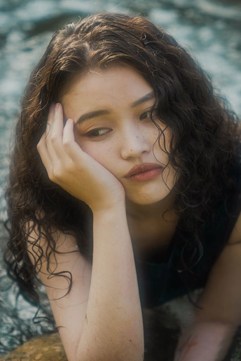 一位年轻女子坐在水中的岩石上 手放在脸上的肖像