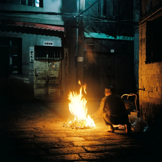 一名男子晚上坐在一栋楼外的小巷里 火焰从楼里冒出来