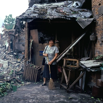 一个拿着扫帚的女人站在被毁房屋的废墟中