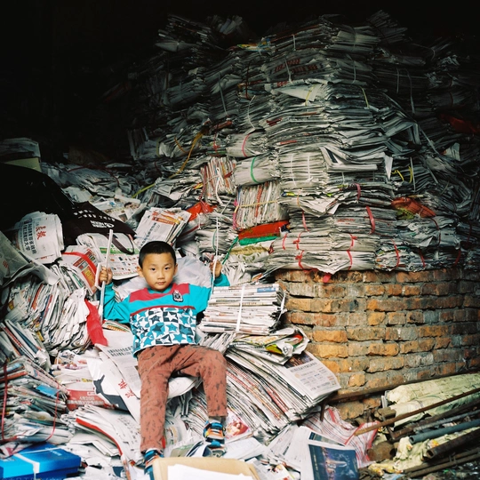 一个小孩坐在一叠报纸上 一个小男孩坐在后面