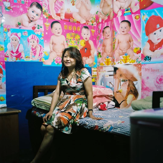 一位年轻女子坐在儿童房的床上 墙上挂着照片 床上坐着一个婴儿