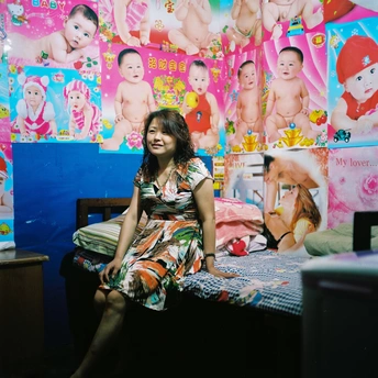 一位年轻女子坐在儿童房的床上 墙上挂着照片 床上坐着一个婴儿