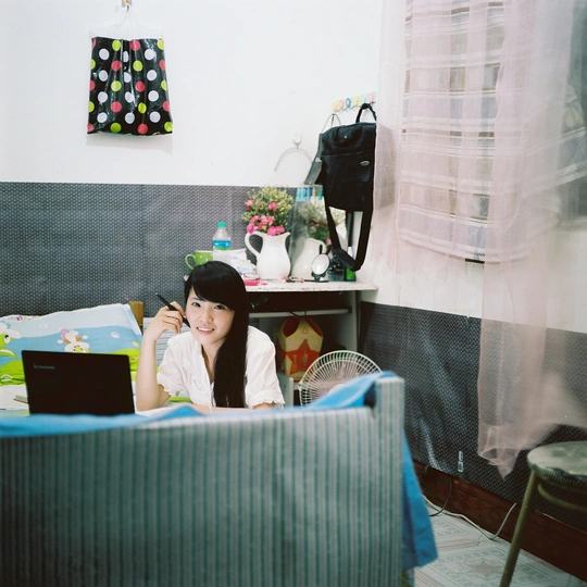 一位年轻女子坐在卧室里 卧室里有床、椅子和桌子 上面有一台笔记本电脑