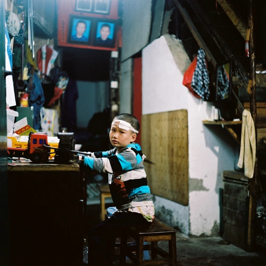 一个小男孩坐在一个小房间的木凳上 房间里有一张小木桌和一把小木椅