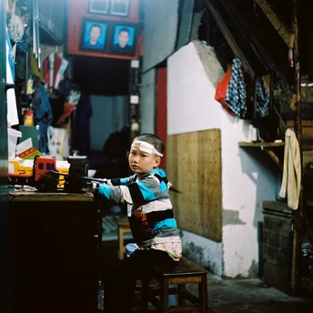 一个小男孩坐在一个小房间的木凳上 房间里有一张小木桌和一把小木椅