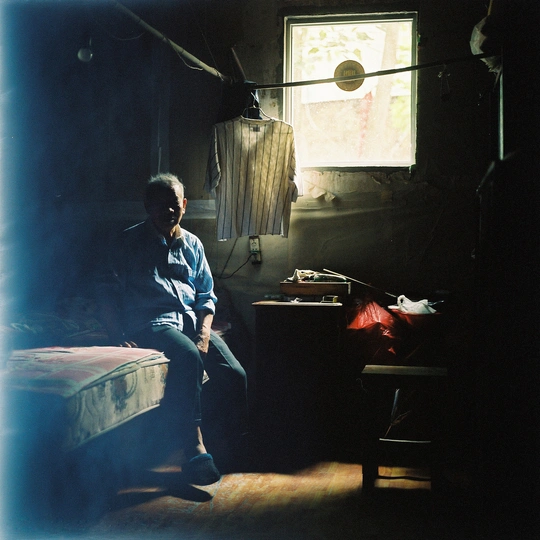 一个男人坐在一个有床和窗户的暗室里的椅子上