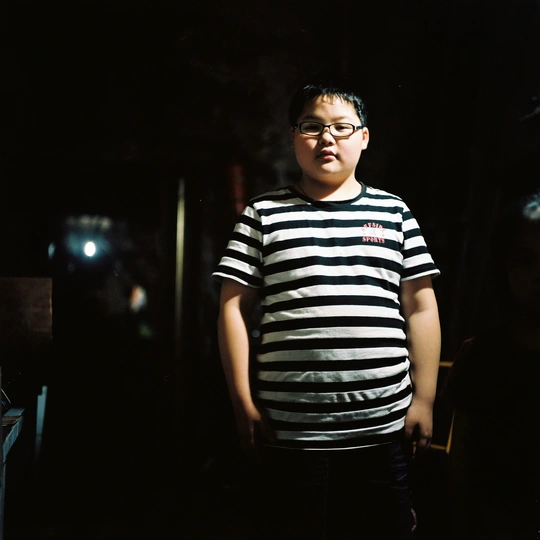 一个戴眼镜、穿着条纹衬衫的年轻人晚上站在黑暗的房间里