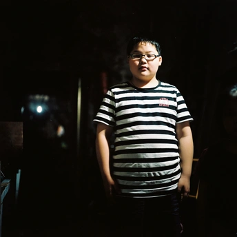 一个戴眼镜、穿着条纹衬衫的年轻人晚上站在黑暗的房间里