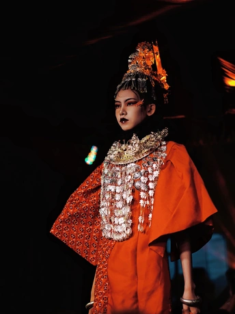 一个穿着橙色传统服装的年轻女孩走在T台上
