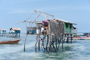一个小村庄的人在海洋的水中站在木桩上 背景中有一艘船经过。