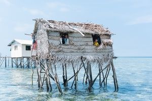 一个人站在海洋中 凝视着建在水上的木桩小屋的窗户。