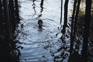 一个年轻男孩在湖中游泳 水中有树木 一个人在水中玩耍。