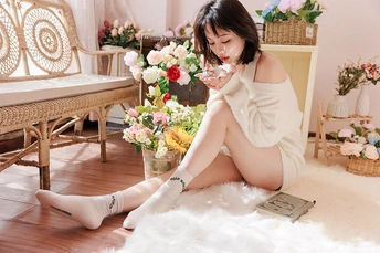 一个穿着白裙子和袜子 喝着一杯葡萄酒 坐在地板上 周围是花的房间的年轻女子。