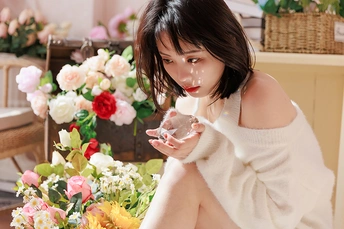 一位年轻女子坐在地板前 面前放着一杯酒和鲜花。