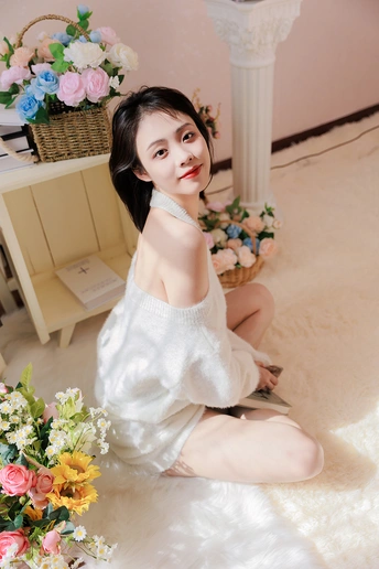 一个穿着白色连衣裙的年轻女子坐在一个小房间里地板上