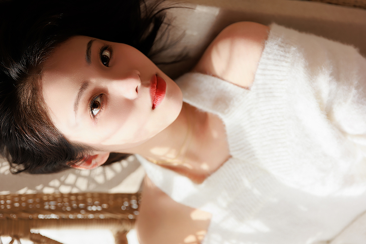 一个穿着白色连衣裙的年轻女子躺在床上 看着相机。